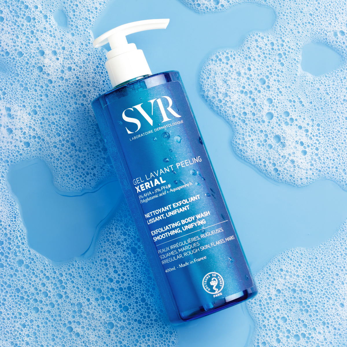 SVR XERIAL Gel Lavant Peeling 400ml bottle with a white pump dispenser, resting on a wet, bubbly blue surface.