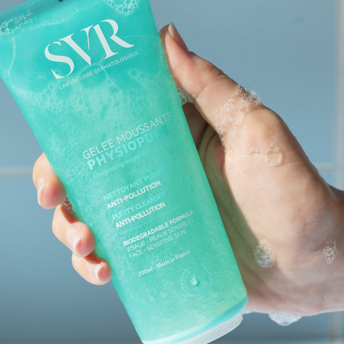 Tube de gelée moussante SVR Physiopure 200ml turquoise translucide tenu en main avec une mousse nettoyante légère.