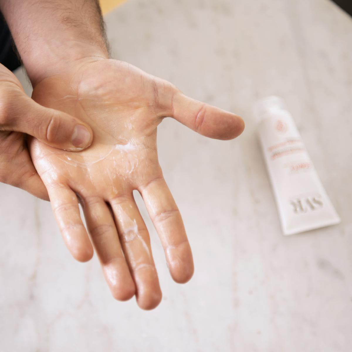 Main appliquée avec la crème réparatrice blanche Cicavit+ SVR sur une surface en marbre clair.