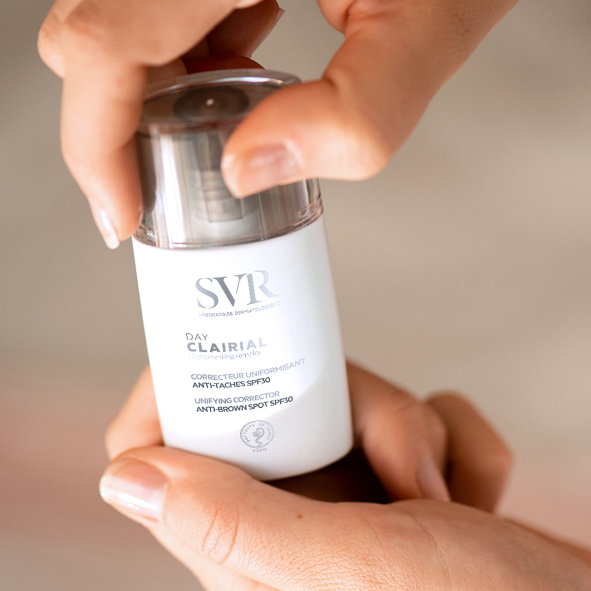Flacon blanc SVR Clairial Day SPF30 tenu en main, correcteur anti-taches pour le visage avec bouchon transparent.