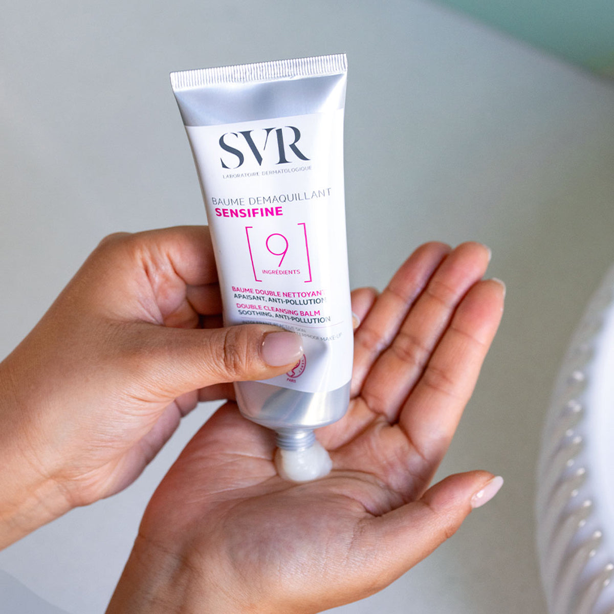 Tube de baume démaquillant SVR Sensifine blanc et argent pressé dans la paume d'une main pour libérer une texture crémeuse.