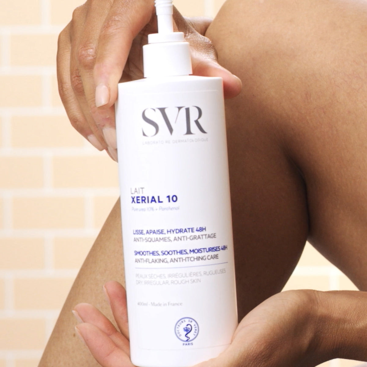 Flacon pompe blanc de lait hydratant SVR Xerial 10 de 400ml tenu par des mains devant une peau nue.