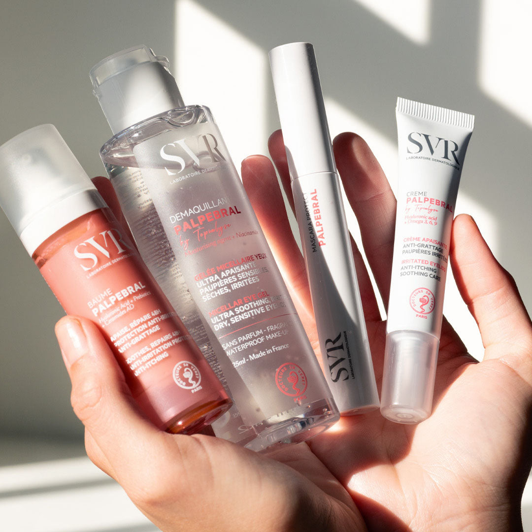 Main tenue tenant trois produits de soin SVR Palpebral : un baume rose, un démaquillant micellaire et une crème apaisante blanche.