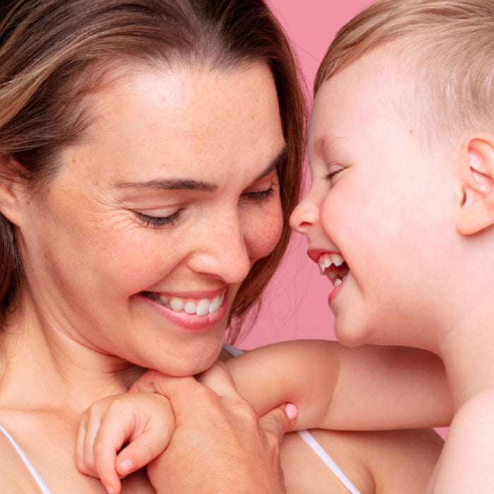 Smiling mother holding her laughing young son against a soft pink background.