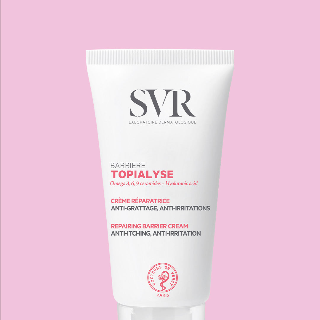 Tube blanc de crème réparatrice SVR Topialyse Barrière sur fond rose, avec texte informatif et logo de la marque.