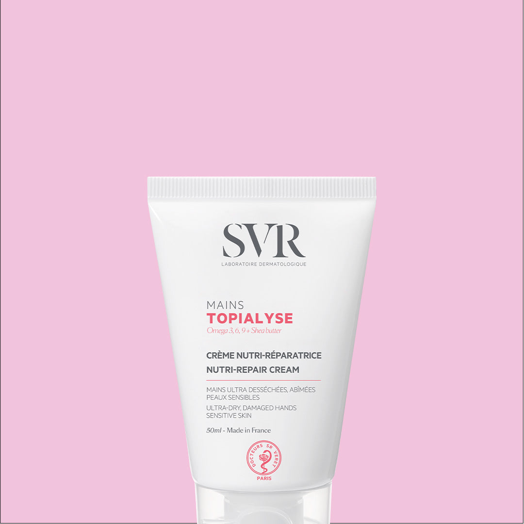 Tube de crème réparatrice SVR Topialyse Mains 50ml sur fond rose, soin nourrissant pour peaux sèches et abîmées.