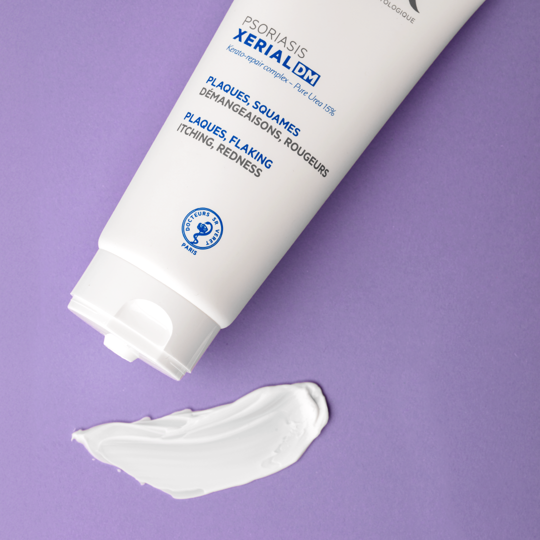 White XERIAL DM Psoriasis cream tube with blue text and a smooth white product swatch on a purple background.