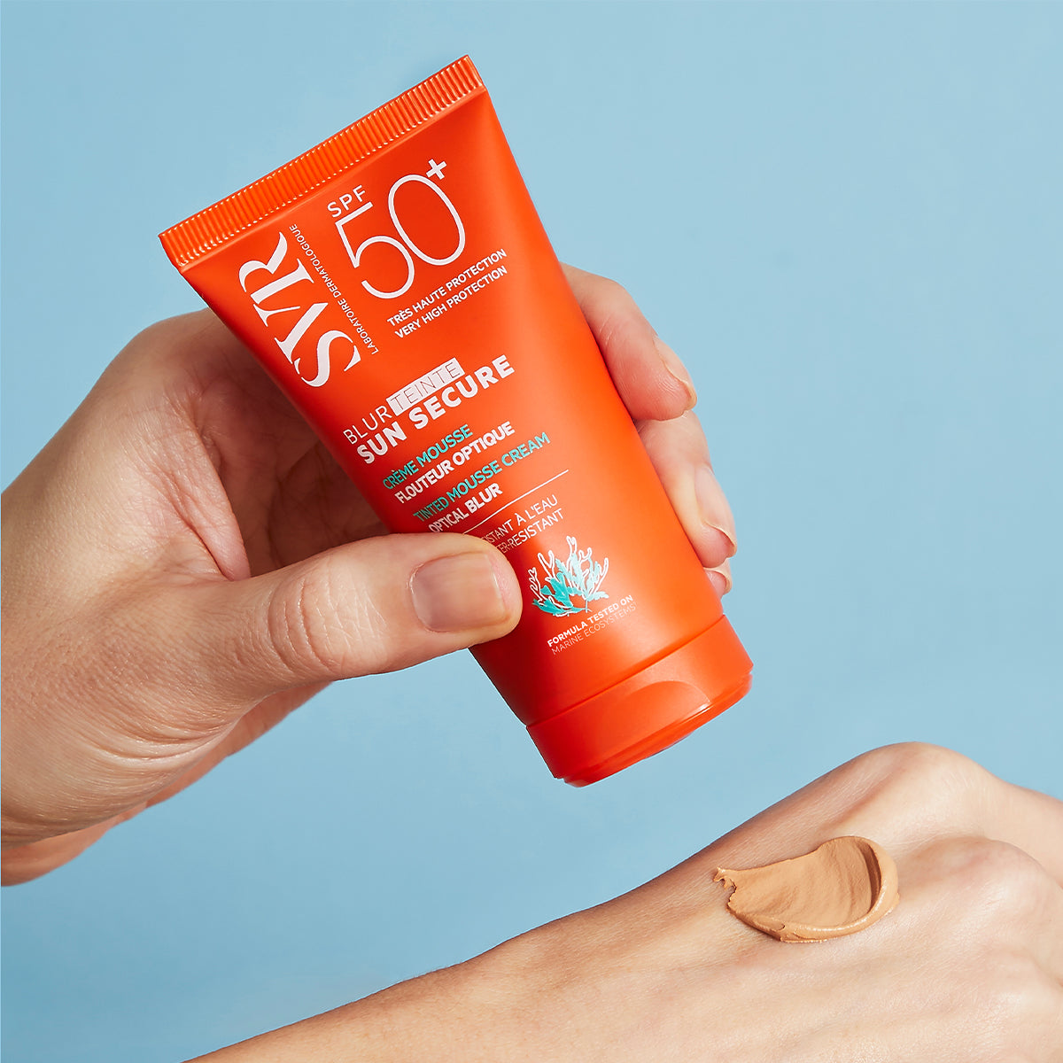 Tube orange de crème solaire SVR Sun Secure SPF50+ appliqué sur le dos d'une main, révélant sa texture mousse teintée.