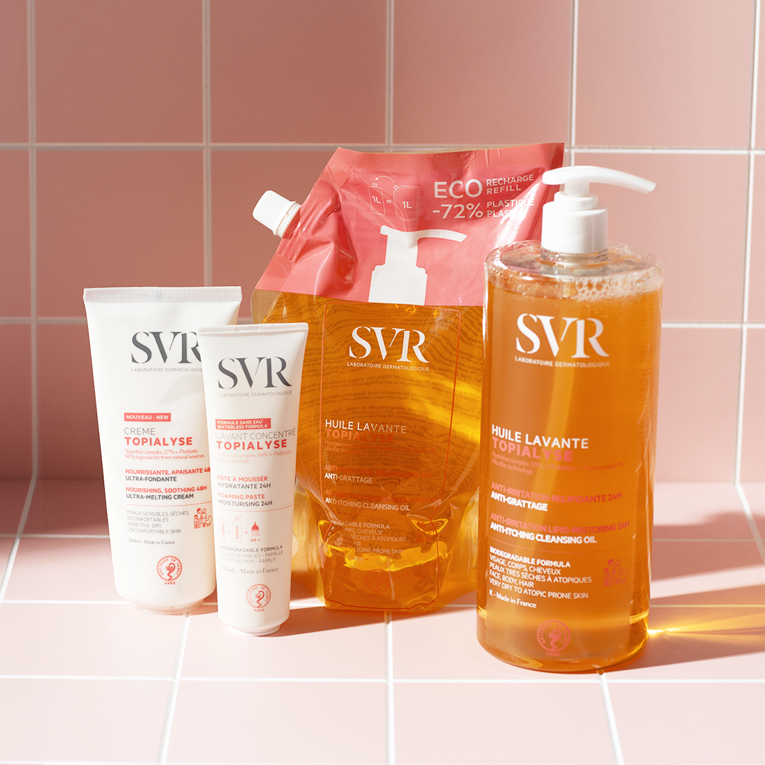 SVR Topialyse skincare range including cleansing oil bottles, a refill pouch, and cream tubes on a pink tiled surface.