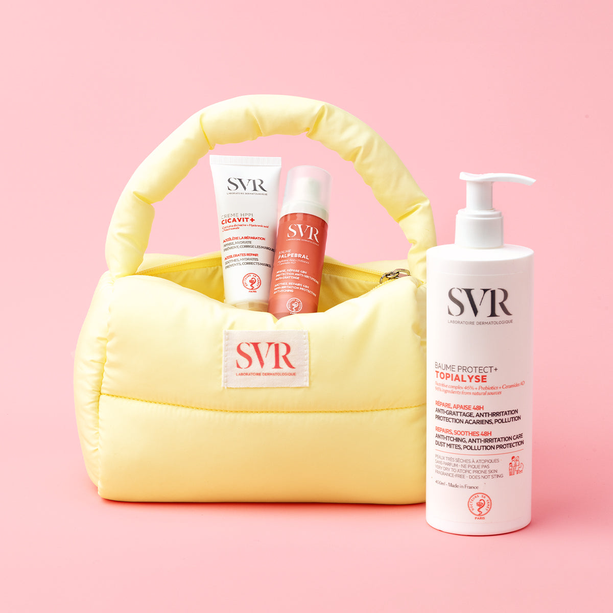 Trousse jaune matelassée contenant des soins SVR pour peaux sèches et abîmées sur fond rose.