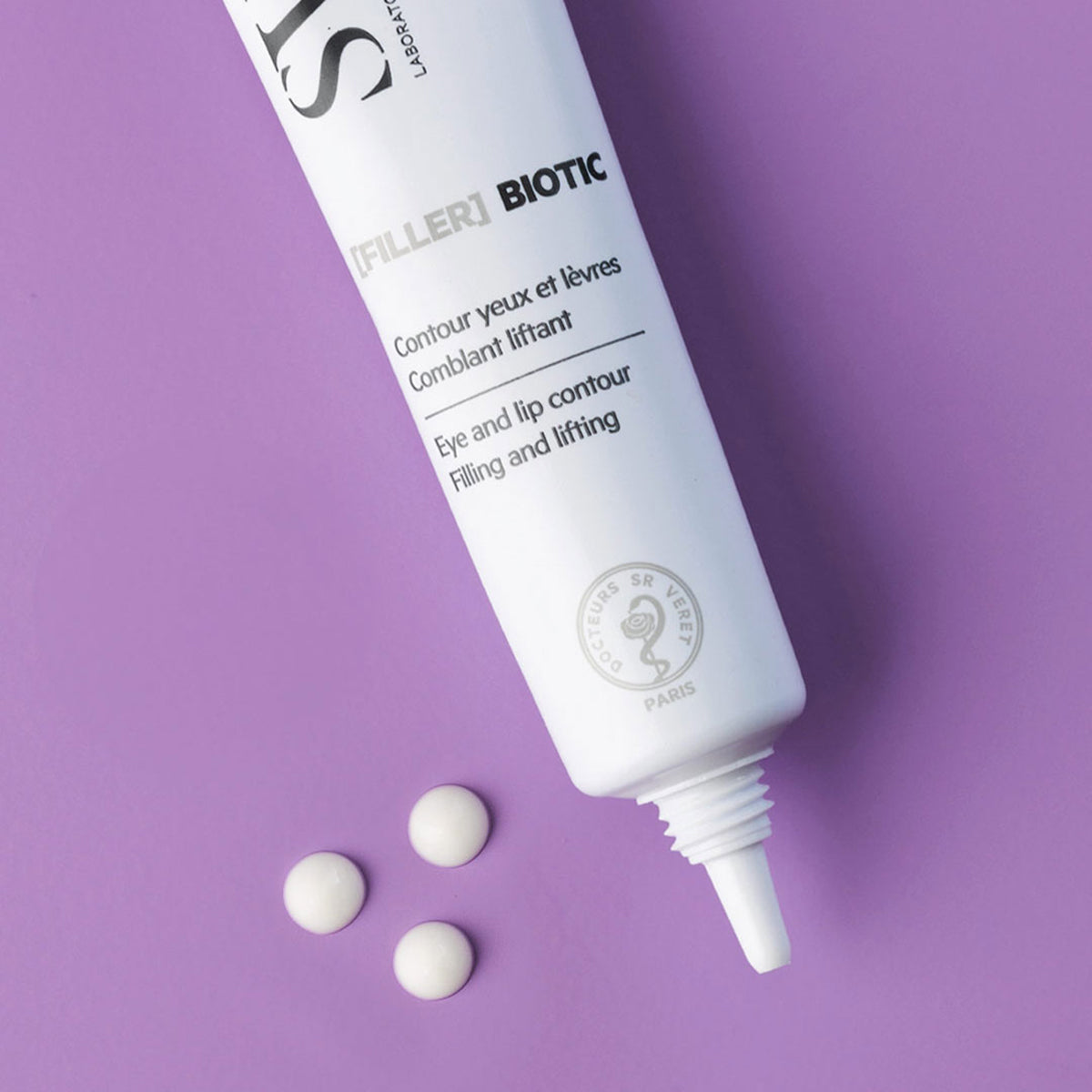 Tube blanc de soin [FILLER] BIOTIC pour le contour des yeux et des lèvres, posé sur un fond violet avec trois gouttes de crème.