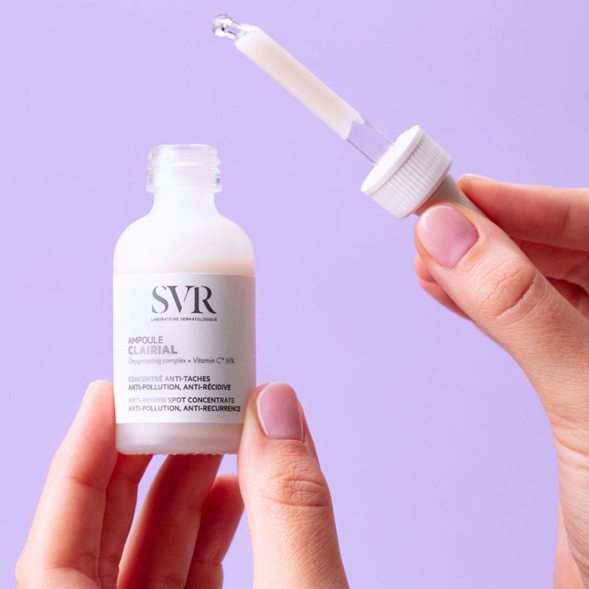 Flacon en verre dépoli SVR Clairial Ampoule tenu en main avec pipette compte-gouttes sur fond violet pastel.