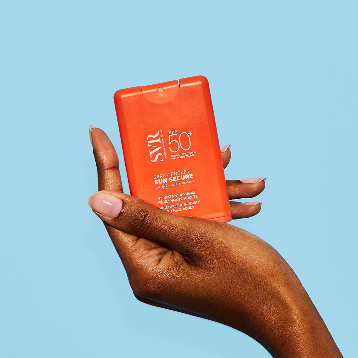 Main tenue en main d'un spray solaire SVR Sun Secure SPF50+ orange au format poche sur fond bleu clair.