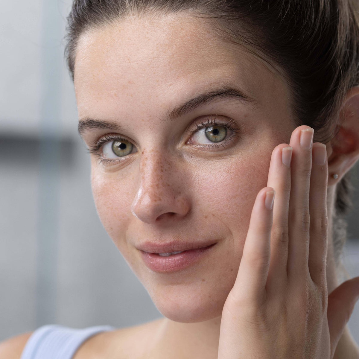 Gros plan sur une femme au teint frais et naturel touchant délicatement sa joue, illustrant une peau nette et purifiée.