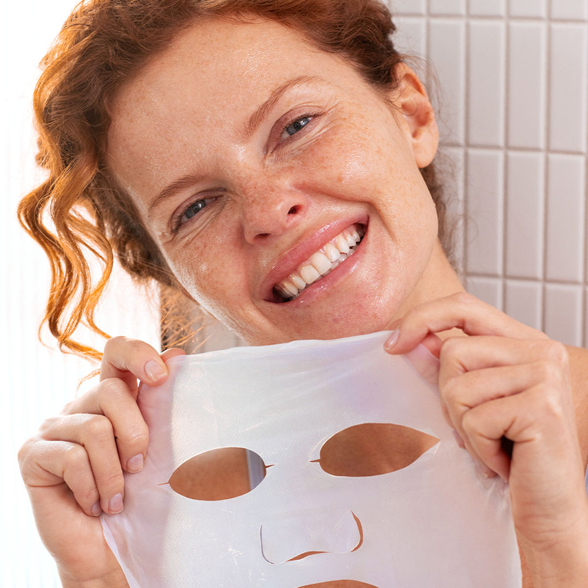 Femme souriante tenant un masque en biocellulose translucide pour le visage, idéal pour l'hydratation intense de la peau.