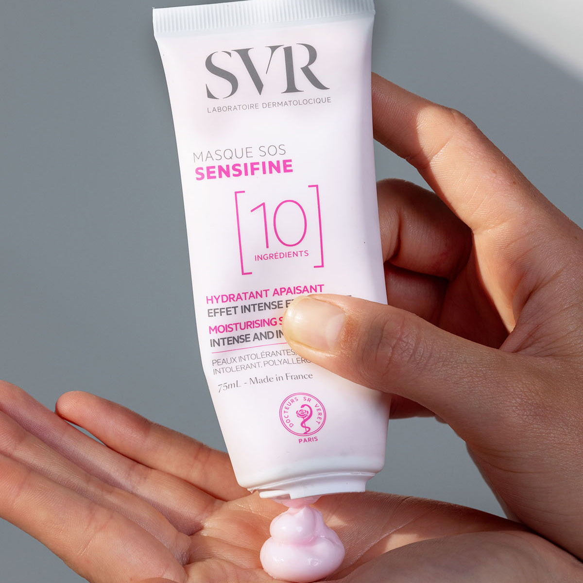 Tube de masque SVR Sensifine SOS blanc et rose pressé dans une main, délivrant une texture crème rose onctueuse.