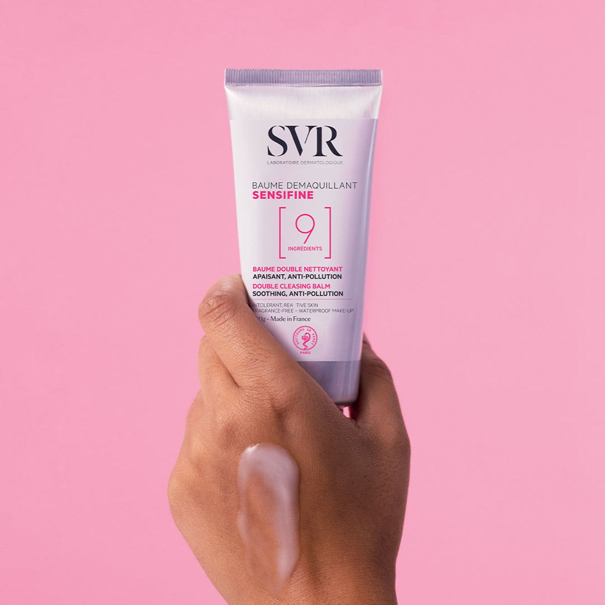 Main tenue en main présentant le tube blanc SVR Sensifine Baume Démaquillant avec une texture huileuse sur la peau.