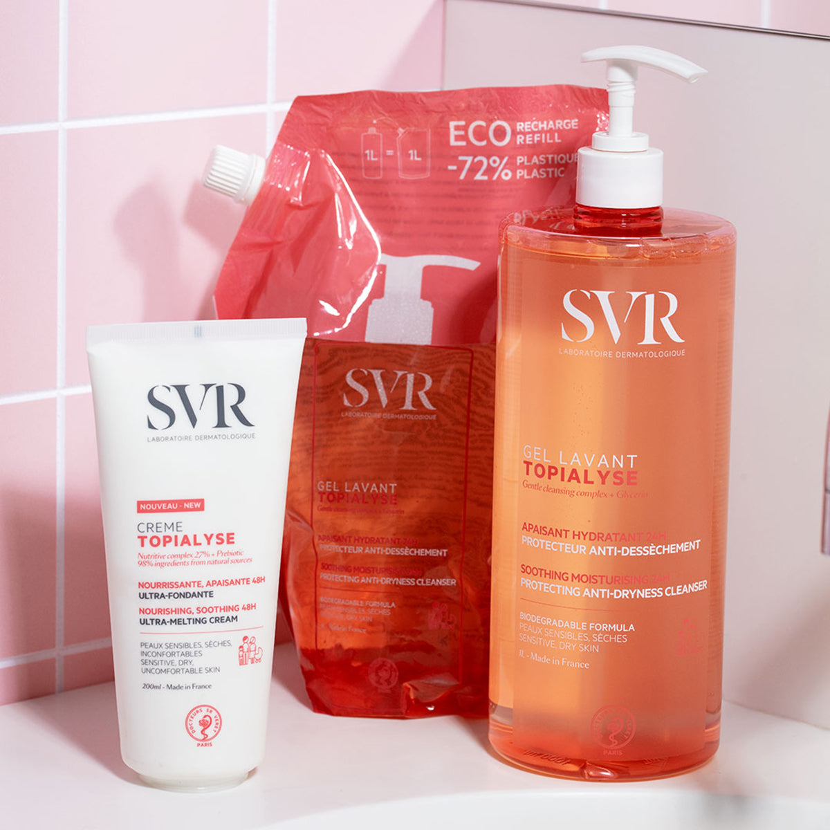 SVR Topialyse gel lavant, éco-recharge et crème sur un comptoir devant un carrelage rose.