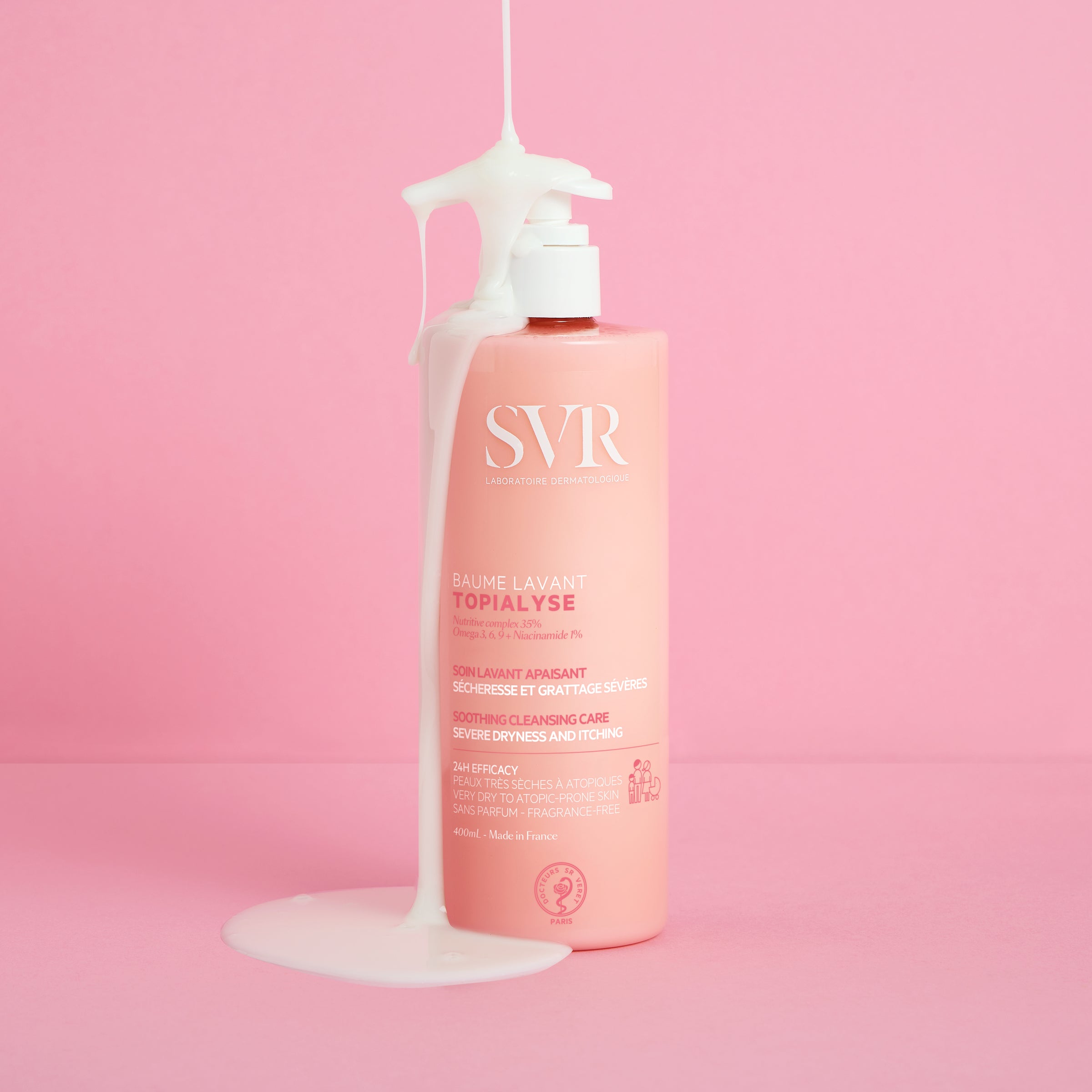 Flacon pompe rose SVR Topialyse Baume Lavant 400ml avec texture crémeuse blanche coulant sur le packaging sur fond rose.