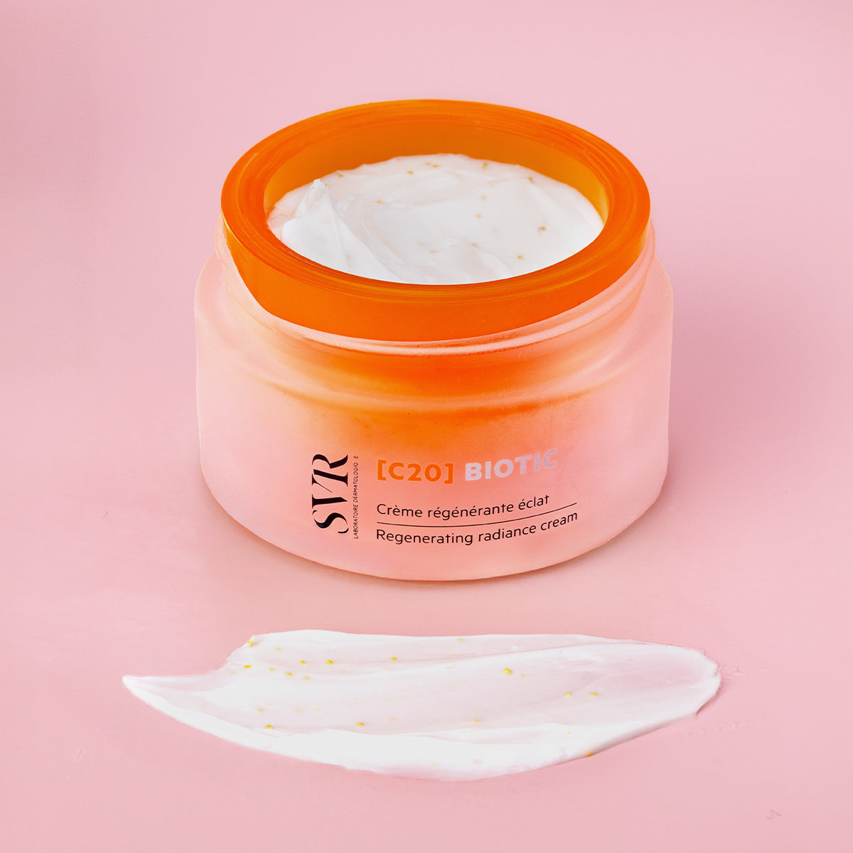 SVR [C20] Biotic regenerating radiance cream in a frosted orange jar with a white textured cream swatch on a pink background.