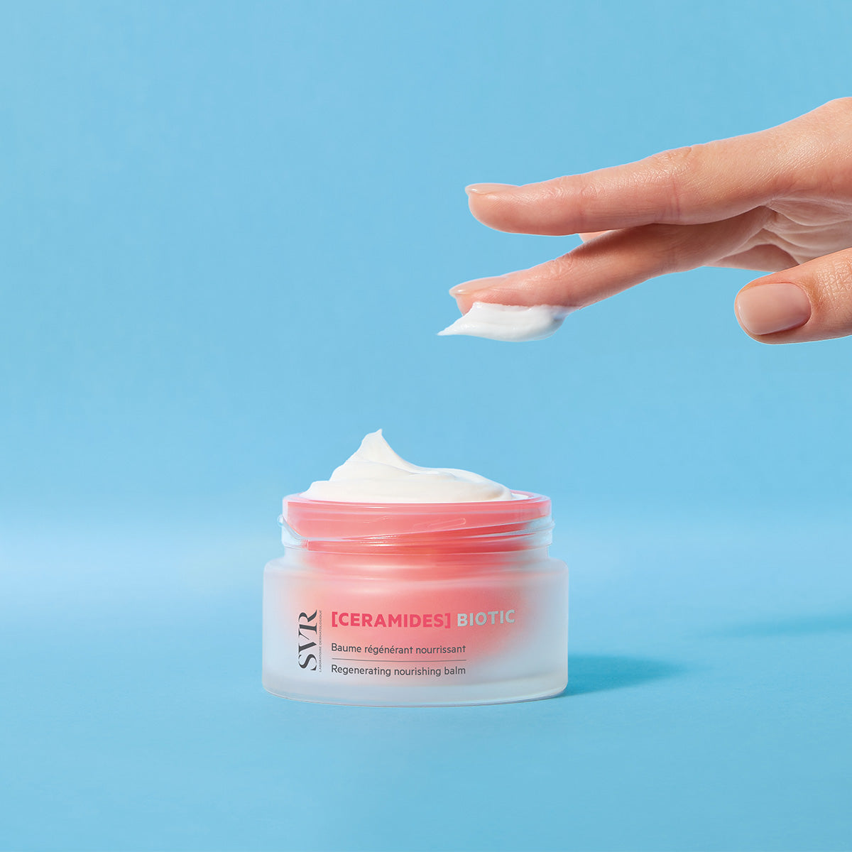 SVR [CERAMIDES] Biotic regenerating nourishing balm in a frosted glass jar with a pink lid against a blue background.