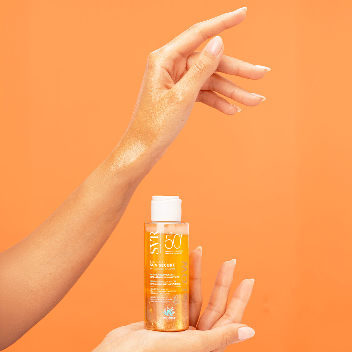 SVR SUN SECURE SPF50+ shimmering sun water bottle held in hand against an orange background with glowing skin.