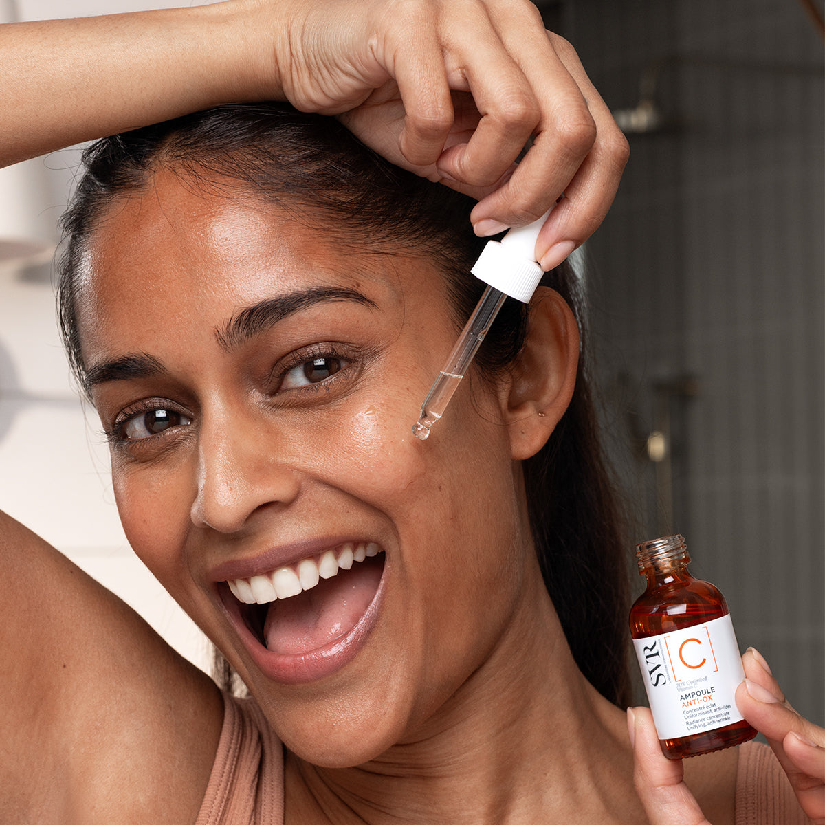 Femme souriante appliquant le sérum SVR Ampoule Anti-Ox avec une pipette sur son visage pour un teint éclatant.