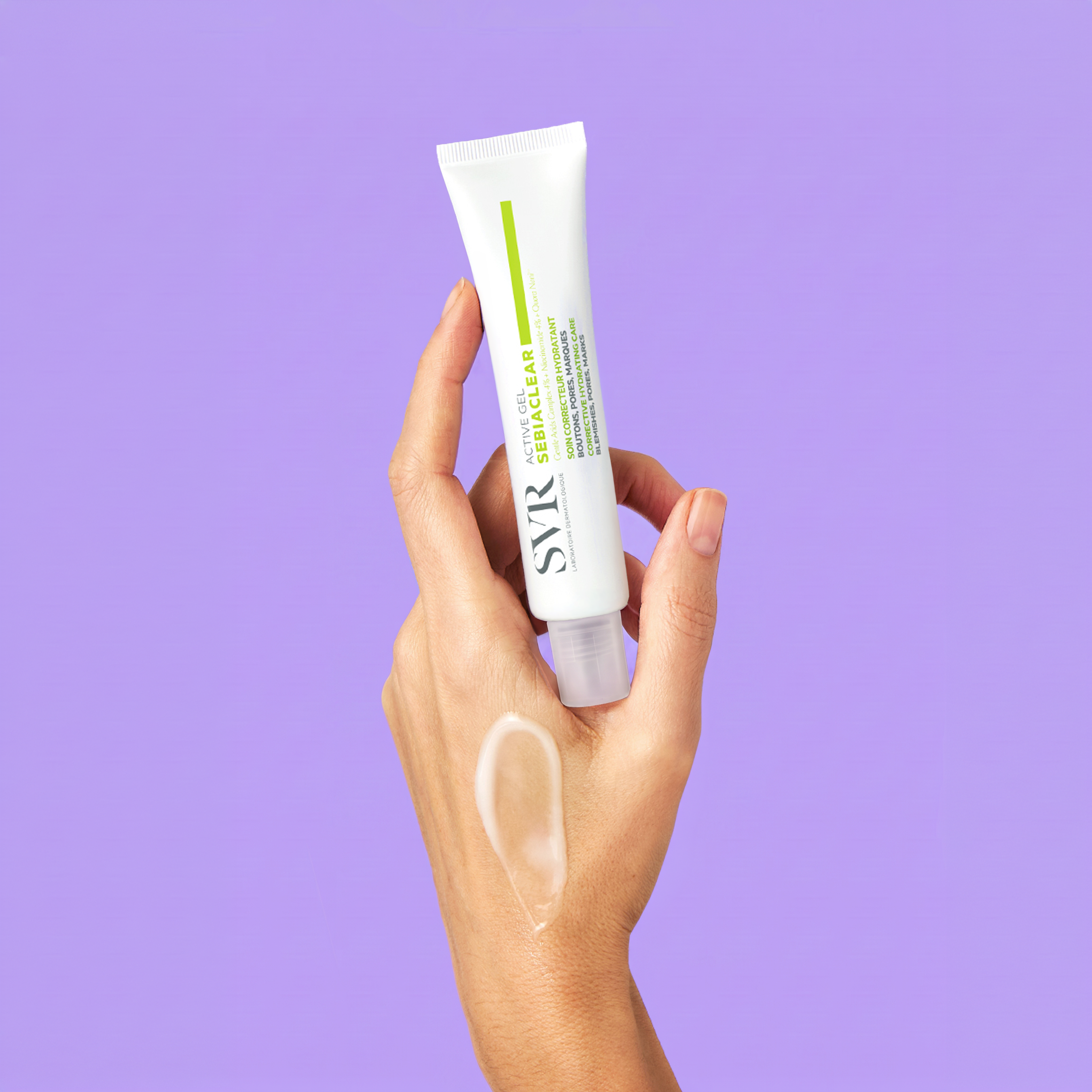 Hand holding a white SVR Sebiaclear Active Gel tube with a cream swatch on the skin against a purple background.